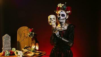 Creepy horror model posing with skull in studio, acting spooky on mexican halloween dios de los muertos. Flirty woman looking like la cavalera catrina to celebrate traditional culture. photo