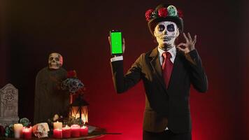 Holy goddess showing smartphone with greenscreen in studio, holding isolated chroma key display background. Scary model using blank mockup copyspace template, wearing suit and hat. photo