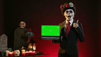 Glamorous holy entity holding laptop with greenscreen display, showing mockup template and blank copyspace in studio. Santa muerte using wireless pc with isolated chroma key screen. photo