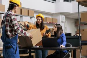 Asian warehouse workers team managing parcels shipping and receiving. Delivery employees checking pick ticket on laptop and scanning cardboard box barcode while working in storehouse photo