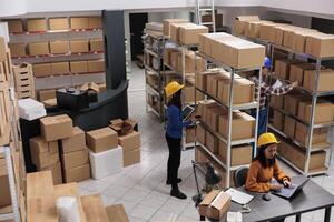 Warehouse employees team working in order fulfillment center. Asian man and women storehouse workers scanning parcels, searching packages and doing inventory on laptop top view photo