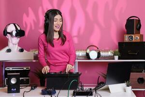 Cheeful musician standing at dj table creating musical performance with remix music using professional mixer console in studio. Asian artist performing electronic song, enjoying nightlife in club photo