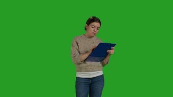Front view of female model looking at clipboard documents, working on analysis and taking notes on papers. Young adult writing information on files, greenscreen backdrop in studio. photo