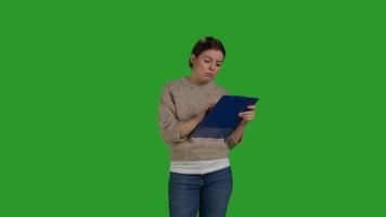 Front view of female model looking at clipboard documents, working on analysis and taking notes on papers. Young adult writing information on files, greenscreen backdrop in studio. photo