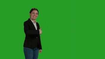 Side view of positive woman giving thumbs up over greenscreen backdrop, expressing like and okay sign in studio. Company female employee in suit doing approval and agreement gesture. photo