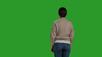 Back view of person showing denial and pushing something aside, expressing refusal and rejection looking displeased. Female model acting discontent and moving object, standing over greenscreen. photo