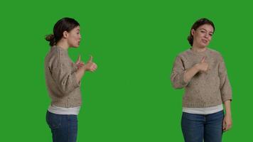 Cheerful model doing thumbs up symbol in studio, expressing approval and like gesture over greenscreen. Female person acting positive and happy, showing agreement and okay good sign. photo