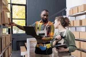 African american manager showing box with customer order while supervisor scanning packages barcode using store scanner in warehouse. Diverse employee working at merchandise inventory photo
