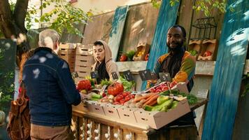 African american vendor working at farmers market counter and selling bio organic fruits and veggies. Young man standing at market stall and presenting fresh natural homegrown products. photo