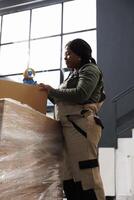 Small business employee putting adhesive tape on carton box, preparing clients packages for shipping in storehouse. Storage room supervisor wearing industrial overall working at online orders photo