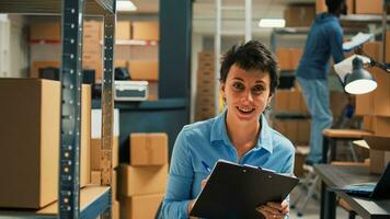 Female entrepreneur taking notes on laptop and analyzing stock of storehouse goods, planning inventory and logistics. Young employee checking quality of merchandise and packages on pc. photo