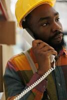 Africna american warehouse worker getting instruction from supervisor on landline phone. Delivery service storehouse employee calling to distribution office to ask merchandise information photo