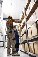 African american warehouse worker scanning parcel for logistics manager. Distribution operator pointing at cardboard box on shelf and storehouse assitant using barcode scanner tool photo