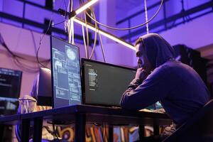 Asian hacker breaking into company database and stealing confidential information. Man cracking complex password and programming ransomware using multiple windows on computer screen photo
