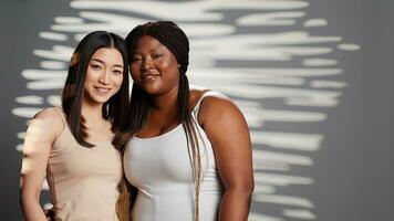 Happy diverse ladies hugging and posing in studio, promoting wellness and bodycare, self acceptance. Flawless young women with different body shapes and skintones showing self love. photo