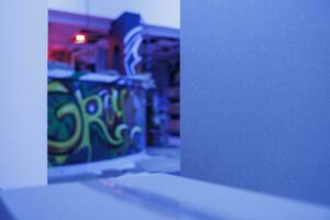 Old crumbling warehouse with purple bright lights, spray paint graffiti glowing under fluorescent lights in abandoned place. Deserted messy space with neon blue glow, rusty warehouse. photo