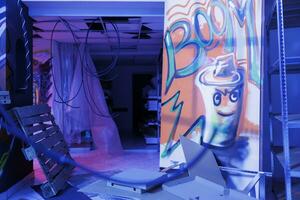 Artistic graffiti illuminated by purple neon lights in deserted old building, empty destroyed space filled with spray paint and fluorescent bright light. Damaged warehouse with art on walls. photo