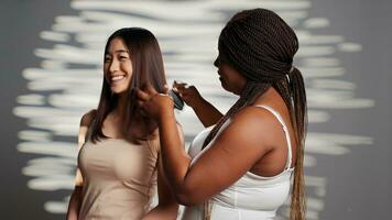 africano americano niña cepillado pelo de asiático amigo en cámara, posando a promover amistad y bienestar. interracial mujer utilizando productos cosméticos, publicidad protección de la piel productos para anuncio campaña. foto