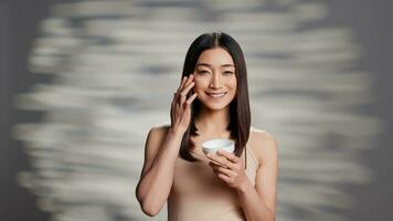 Young radiant person applying moisturizing cream to promote skincare routine and uplifting products. Beauty model using face serum and moisturizer for new cosmetology ad campaign. photo