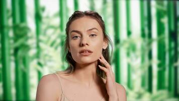 Positive glowing adult with radiant bare skin posing in studio over background with bamboo trees. Cheerful confident woman advertising beauty products and skincare routine on camera. photo