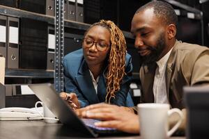 Detective teaching law student analyzing crime case using laptop. African american man and woman investigators searching information on computer and examining police report together photo