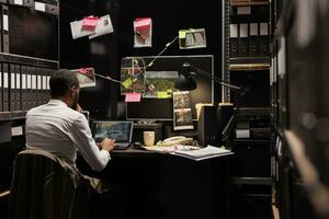 Private detective checking surveillance photos on laptop, spying on suspect for client. African american man investigator sitting at desk, analyzing photographs on computer screen