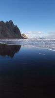 Massive vestrahorn mountains connect with ocean, fantastic nordic setting with unique black sand beach. Icelandic stokksnes peninsula with huge cliffs and hills, breathtaking scenic route. photo