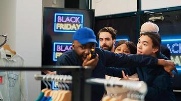 Black friday seasonal sales event at shopping center. Security guard calling for backup on walkie talkie radio, pushing back aggressive group of shoppers trying to reach special offers. photo