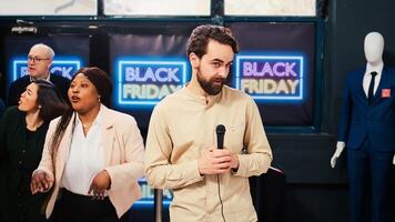 TV reporter standing in front of camera reporting breaking news from black friday event at local shopping center. News journalist broadcasting from crowded clothign store at mall. photo