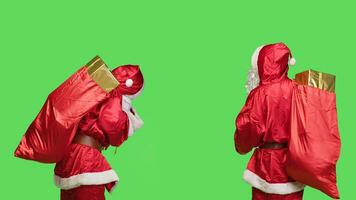 Young man portraying santa claus on greenscreen backdrop, preparing to deliver presents to children around the world. Father christmas with huge red sack of toys, december season. photo