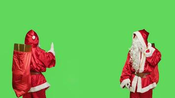 Saint nick pushing object to left or right sides, showing dismiss gesture over greenscren in studio. Santa claus embodiment doing rejection sign, christmas eve celebration concept. photo