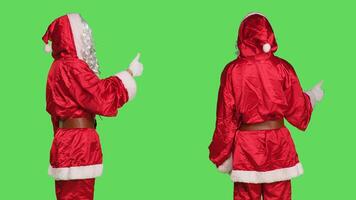 Saint nick shows thumbs up symbol while he wears festive costume with white beard, cosplaying father christmas for winter holiday. Person in red suit doing like gesture for agreement, greenscreen. photo