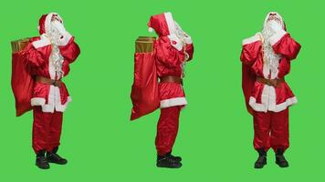 Sleepy person in santa suit yawning against full body greenscreen, feeling exhausted of carrying bag with presents and toys for december holiday. Saint nick embodiment feeling tired. photo