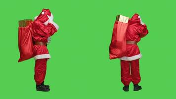 Saint nick with migraine carries sack, trying to deliver gifts boxes to children on time for christmas eve holiday. Unwell main character having painful headache, full body greenscreen. photo