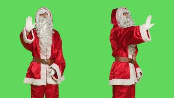 Father christmas cosplay raise palm to say no, showing stop sign in studio with greenscreen. Man in santa claus costume doing rejection and refusal symbol on camera, christmas eve concept. photo