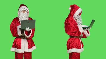 Saint nick using laptop on videocall, talking to people on online videoconference meeting and browsing online page. Modern person holding pc wireless on chat on teleconference, greenscreen. photo