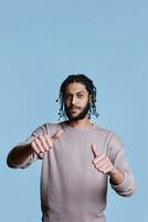Cool arab man showing two thumbs up gesture and looking at camera with raised eyebrows. Confident serious youn adult person standing making like symbol with fingers portrait photo