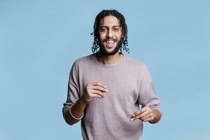 Happy smiling arab man snapping with fingers, feeling music beat and looking at camera. Cheerful young person with carefree facial expression dancing and moving while listening to song portrait photo