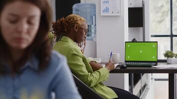 Executive assistant analyzing green screen display on pc, using laptop with chroma key copyspace display. Office employee looking at isolated mockup screen in business coworking space. photo