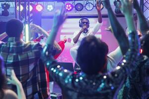 African american musician on stage singing and entertaining crowd in nightclub. Young man dj in headphones speaking to clubbers in microphone and performing at party in club photo