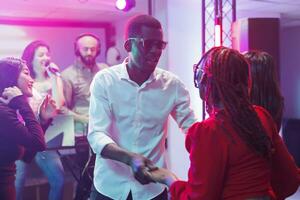 Couple partying on dancefloor in nightclub at discotheque and enjoying nightlife entertainment. African american man and woman dancing while attending electronic music performance photo