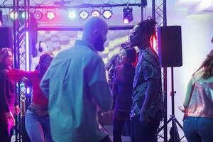 People partying on crowded dancefloor in dark nightclub illuminated with spotlights. Diverse young clubbers dancing, having fun at discotheque while enjoying nightlife in club photo