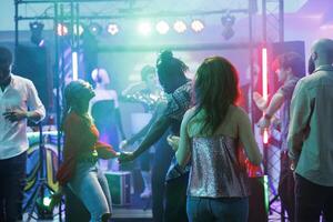 Party dancers making moves on dancefloor while having fun and relaxing in nightclub. People attending discotheque and dancing while enjoying music in club illuminated with stage lights photo