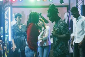 African american man and woman couple dancing and battling while clubbing at discotheque. Young dancers showing improvised moves on dancefloor for people in dark nightclub photo