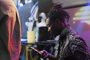 Young african american man using smartphone while resting in nightclub. Clubber scrolling social media and online pages on mobile phone while relaxing at discotheque party in club photo