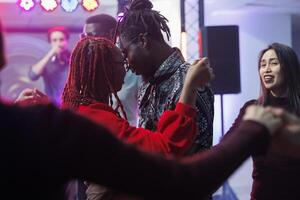 Young couple in love dancing together and hugging in crowded nightclub. African american man and woman embracing while moving and showing affection on dancefloor surrounded with clubbers photo