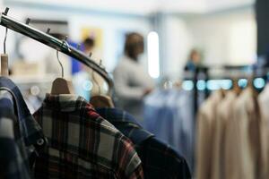 Casual plaid shirts hanging on rack closeup in empty clothing store with blurred background. Stylish outfit on hangers in shopping mall fashion department with no people indoors photo