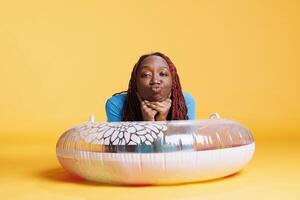 Happy person sitting on inflatable ring, having fun on the floor in studio. Young woman smiling and acting silly on camera with float ring, joyful excited female model laying down. photo