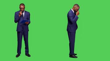 Businessman thinking about company information in studio, brainstorming new ideas and taking notes on clipboard papers. Young office employee wearing formal suit and being pensive. photo