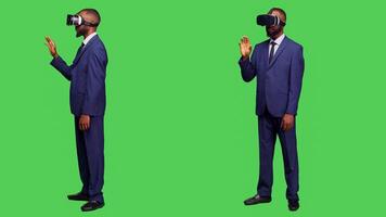 Corporate employee using vr headset on camera, working with virtual reality glasses and 3d simulation in studio. Young entrepreneur with modern device on full body green screen. photo